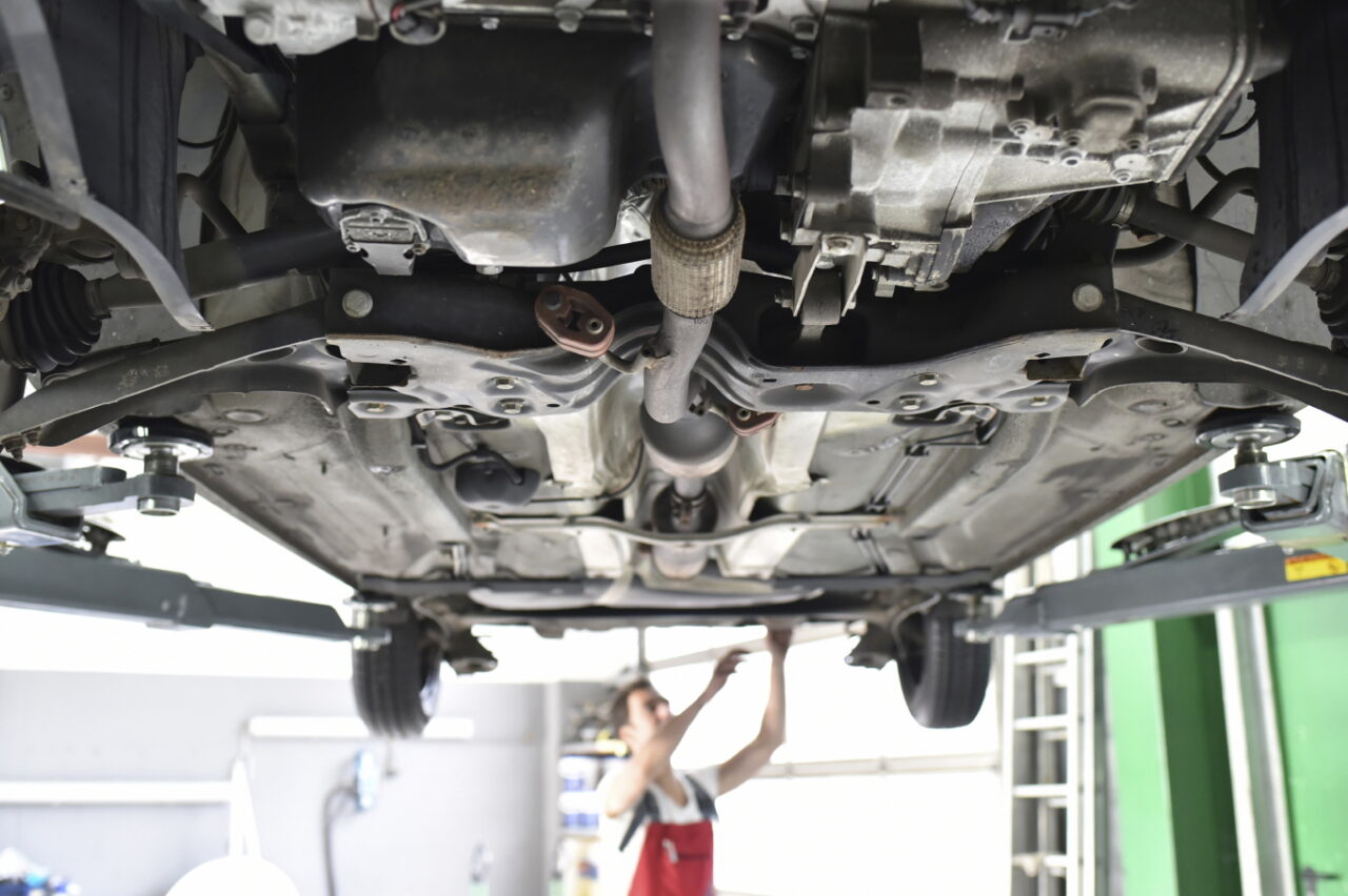 Car mechanic working in repair garage, checking underbody of a car