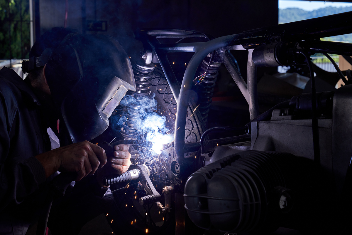 Side view of unrecognizable man in welding helmet in process of repairing motorbike while working in professional workshop