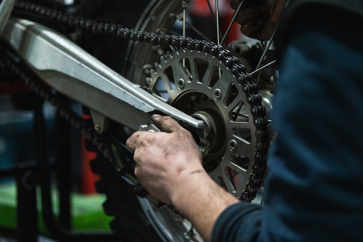 Crop anonymous male auto mechanic with dirty hands fixing wheel while repairing retro motorbike in workshop