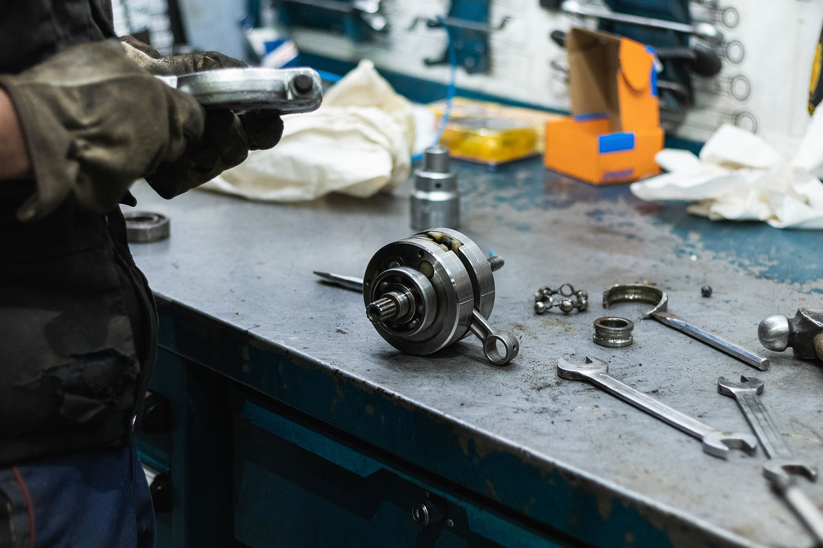 Crop unrecognizable male mechanic in dirty protective gloves holding crankshaft bearing removal tool while working in garage at table with various instruments