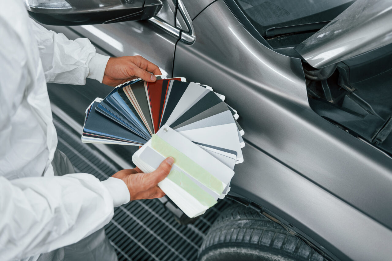 Holds cards with different colors. Caucasian automobile repairman in uniform works in garage.