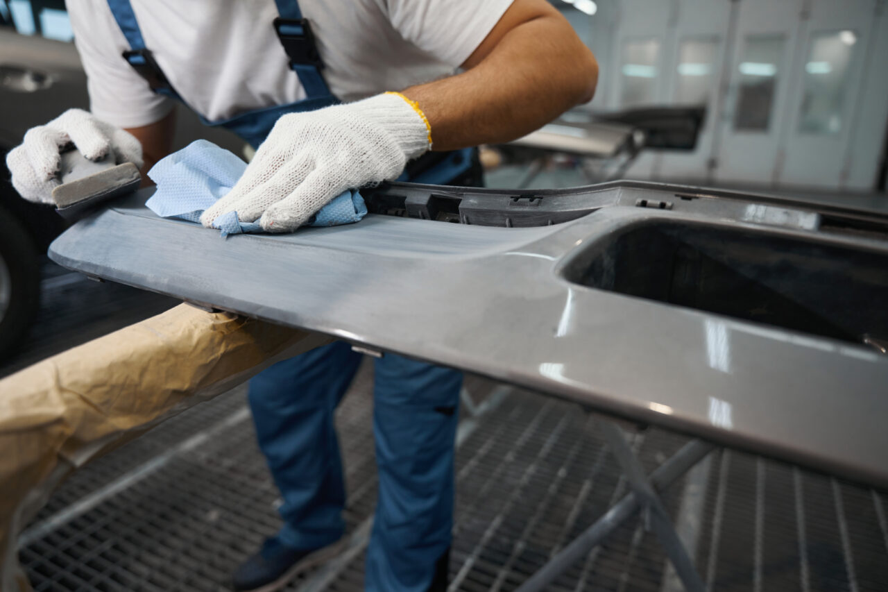 Fitter in protective gloves holding grinding tool and cleaning surface before priming in tire fitting