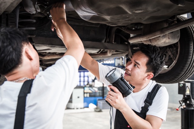 Two mechanic was checking the car suspension. Vehicle raised on lift at maintenance station. Car in service station with two men repair. Car mechanic working at automotive service center.